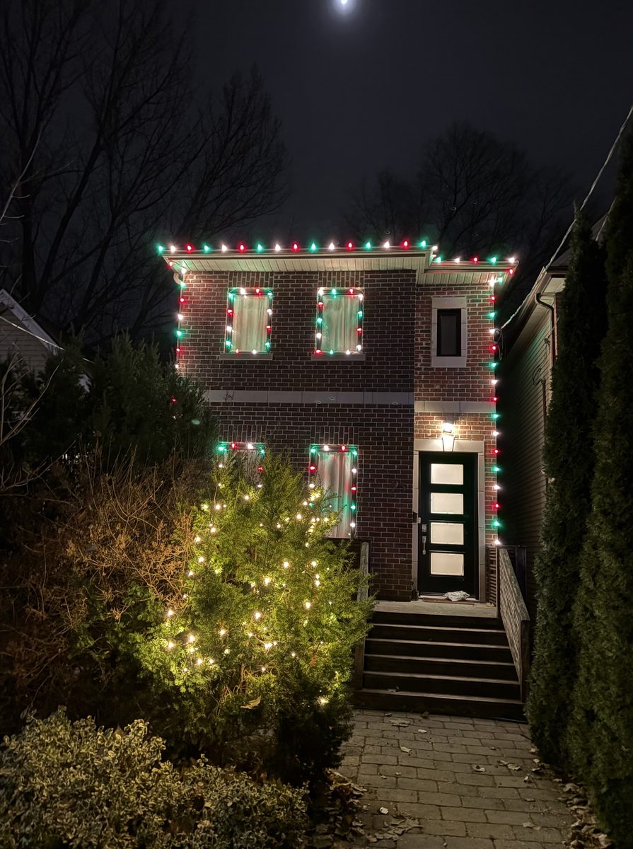 The same house with red, green and white lights on the roofline, windows and tree