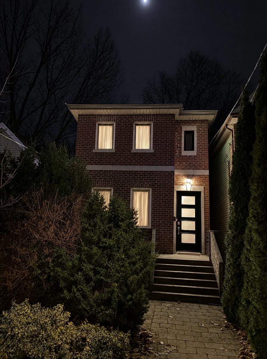 A narrow brick house and front tree at night with no lights