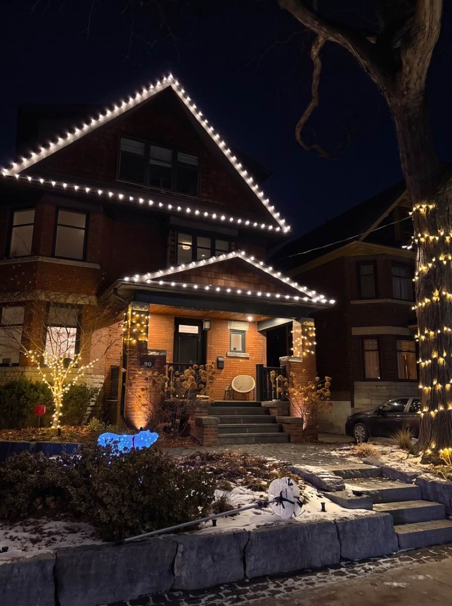 The same house with lights on the roofline, porch and tree