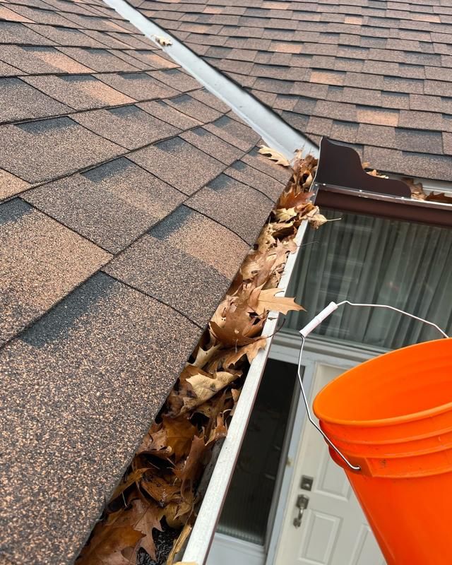 Roof gutter packed with oak leaves beside an orange bucket