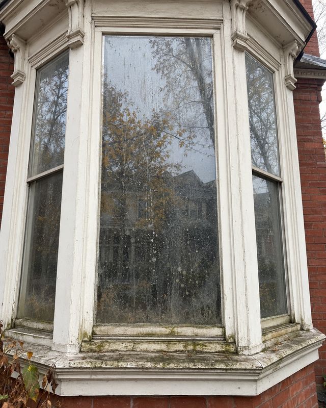 Three sided bay window on a red brick Victorian, glass spotted and the sills green with grime before cleaning