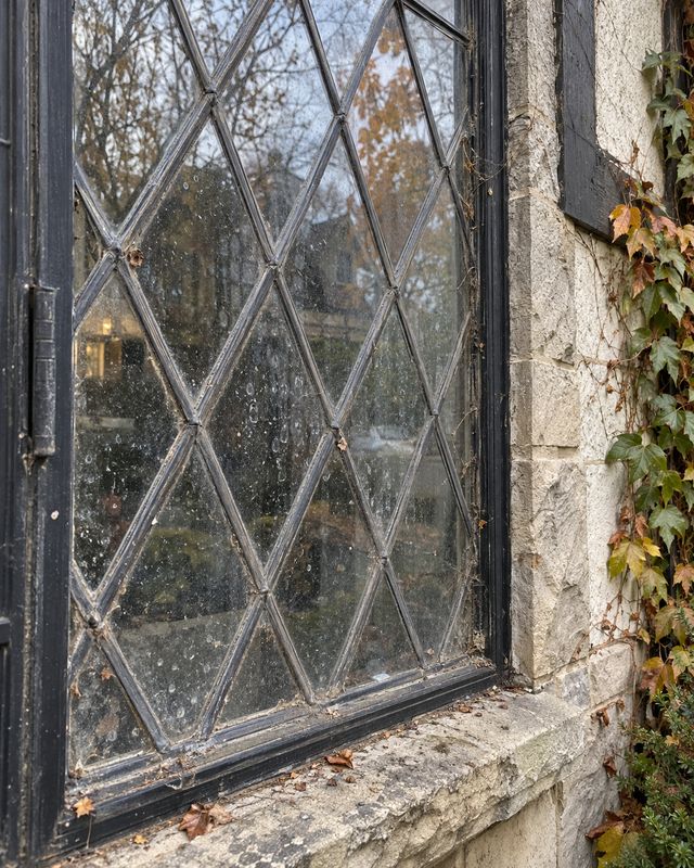 Leaded diamond pane casement window on a stone Tudor house, glass spotted and cobwebbed before cleaning